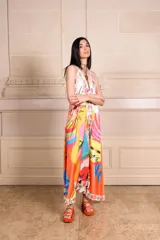 Vestido largo de seda con estampado vibrante y multicolor que incluye motivos frutales y caras sonrientes. Diseño de solera con escote halter anudado al cuello y falda amplia.