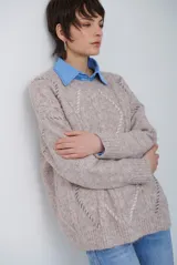 Buzo de punto color beige con diseño de trenzas y costuras decorativas en contraste que forman rombos. Presenta cuello redondo, mangas largas y puños acanalados.
