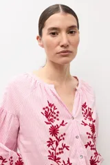 Blusa de manga larga con estampado de rayas verticales en tonos celestes y blancos. Presenta un escote en V con cierre frontal de botones y detalles de bordados florales en color crema en el frente y en los puños.