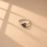 Anillo de plata 925 con diseño de nudo central que sostiene una pequeña piedra oscura.