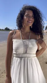 Vestido largo de gasa color marfil, con escote recto, tirantes finos y falda con caída fluida. Presenta drapeado en el busto y detalle de canutillos bordados en tirantes y cintura.