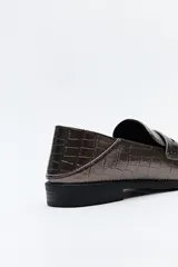 Mocasín de cuero sintético negro con punta cuadrada, detalle de costuras visibles en la capellada y taco bajo.