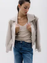 Chaqueta corta estilo biker color beige, confeccionada en piel sintética. Presenta cierre asimétrico frontal, bolsillo con cierre a la vista y bolsillo con solapa, cinturón con hebilla en la cintura.