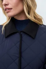 Campera larga capitoneada en color azul marino, con diseño de rombos, cuello camisero en contraste, cierre frontal y bolsillos laterales de parche.