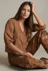 Blusa de algodón color marrón con cuello en V, mangas tres cuartos con puños elásticos y detalles de encaje y alforzas en el frente.