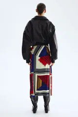 Pollera larga con diseño cruzado efecto pañuelo y brillo sutil. Presenta un estampado geométrico multicolor en tonos azul, rojo y crudo con detalles de cadenas.