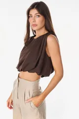 Top cropped satinado de color marrón, con diseño sin mangas, cuello redondo y drapeado frontal que genera volumen.