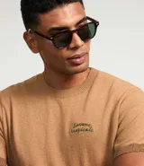 Remera de manga corta color marrón claro, confeccionada en algodón, poliéster, viscosa, elastano y poliamida. Presenta cuello redondo, corte regular y estampa frontal con palmeras y texto "Savane Tropicale".