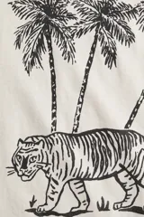 Remera de punto de algodón color beige claro, con cuello redondo y manga corta. Presenta un estampado gráfico en negro que incluye tres palmeras, un tigre caminando y el texto "COASTAL" y "OASIS" enmarcado.