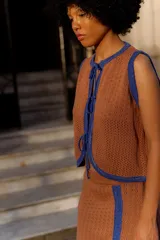 Chaleco tejido sin mangas, color negro, con textura brillante (lurex) y ribetes en azul. Presenta un escote redondo y se ata al frente con cordones.