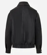 Campera de estilo urbano con corte oversized, confeccionada en poliuretano con base de poliéster. Presenta cuello clásico, cierre frontal con botones a presión, mangas largas y dos bolsillos frontales con tapa. El bajo cuenta con elástico para un mejor ajuste.