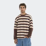 Remera de manga larga con diseño de rayas horizontales en tonos marrón, beige y azul. Presenta un corte boxy holgado y un efecto de superposición en las mangas con puños en color marrón sólido. Incluye un logo bordado en el pecho y en la manga derecha.