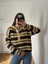 Sweater tipo chomba de tejido de punto con diseño de rayas horizontales en tonos marrón y amarillo. Presenta cuello polo con tapeta de botones frontal y mangas largas.