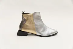 Botín corto de cuero plateado y dorado, con cierre lateral y taco geométrico negro.