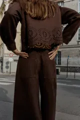 Pantalón culotte marrón de tiro alto con efecto ante, bolsillos delanteros y traseros, pernera ancha y corta. El bajo está troquelado con un diseño floral. Cierre frontal con cremallera y botón.