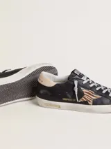Zapatilla Golden Goose modelo Super-Star, confeccionada en cuero vacuno negro con efecto desgastado. Presenta la clásica estrella lateral de pelo con patrón animal print tipo cebra, contrafuerte en cuero nude y cordones con hilo plateado. Suela de goma con acabado envejecido y detalles con inscripciones doradas.
