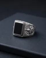 Anillo de acero tipo sello con piedra central rectangular color negro y diseño lateral grabado con motivo de flor de lis.