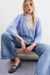 Cardigan de punto color celeste con frente decorado con lentejuelas, escote en V, cierre frontal con botones y mangas largas con terminaciones en punto rib.