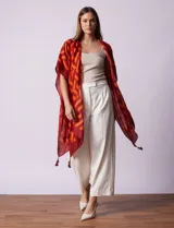 Kimono ligero de poliéster con estampado geométrico en tonos rojo oscuro y naranja. Presenta mangas anchas y terminación con borlas en los ruedos.
