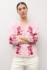 Blusa de manga larga con estampado de rayas verticales en tonos celestes y blancos. Presenta un escote en V con cierre frontal de botones y detalles de bordados florales en color crema en el frente y en los puños.