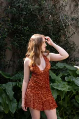 Vestido corto negro con escote en V profundo, estilo halter con tiras para atar al cuello. Presenta un diseño ajustado en el busto con tiras ajustables bajo el mismo que se cruzan y anudan en la espalda, y falda con volado en el ruedo con detalle de encaje.