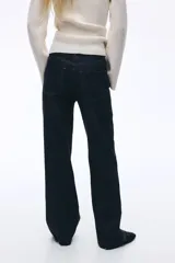 Jean de tiro alto con corte wide leg, confeccionado en denim rígido de color azul oscuro. Presenta diseño de cinco bolsillos, cierre con botón y ruedo deshilachado.