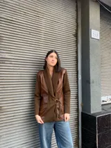 Chaqueta de punto color marrón con cuello de punto acanalado y solapas de cuero. Presenta un cinturón de tela con hebilla dorada y bolsillos de cuero con detalles de cordones.