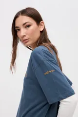 Remera de manga corta color azul, con calce clásico y tajos laterales. Presenta un bordado pequeño en el pecho con el texto 'UNIFORM STUDIO LAB' y un detalle bordado en la manga. Confeccionada en algodón lavado con textura suave.