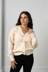 Saco de punto color manteca con cuello en V, cierre frontal de botones y apliques de flores bordadas en relieve. Presenta diseño de trenzas y puños acanalados.