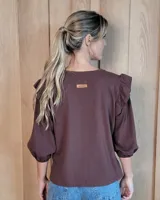 Remera de algodón color marrón chocolate, con cuello redondo y mangas tres cuartos abullonadas con detalle de volados en los hombros y puños elásticos.