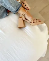 Sandalia de cuero vacuno color beige, con plataforma y taco cuadrado alto. Presenta un diseño de tiras cruzadas en el empeine y cierre con pulsera ajustable al tobillo.