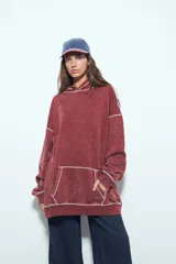 Buzo con capucha de calce relajado, confeccionado en tela con efecto lavado desgastado. Presenta costuras a la vista en color contrastante y un bolsillo frontal tipo canguro.