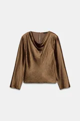 Blusa de manga larga con cuello fluido tipo drapeado y abertura en los puños. Presenta un acabado satinado con textura y cierre posterior con cremallera oculta.