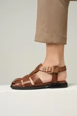 Sandalia baja de cuero color marrón con tiras entrecruzadas y hebilla dorada al tobillo.