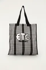 Bolsa tote de diseño amplio a rayas verticales en blanco y negro, con asas de hombro negras y aplique frontal bordado con letras.