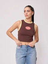 Musculosa marrón tipo tank top con ribetes amarillos en el cuello y las sisas. Presenta un parche estampado frontal ovalado de la marca Rusty Shop.