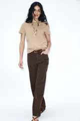 Jeans de tiro alto color azul oscuro, con cinco bolsillos, pernera ancha y nervio marcado en el delantero. Incluye un cinturón fino de cuero sintético marrón con textura de cocodrilo. Cierre frontal con cremallera y botón.