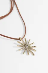 Collar de estilo boho con cordón largo de gamuza color tostado y dije central de metal plateado con forma de sol texturado.