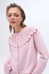 Saco color crudo confeccionado en tejido de punto, con cuello redondo y cierre frontal de botones. Presenta un canesú superior y puños acampanados con detalles de tejido calado y terminaciones de crochet.