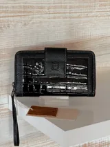Billetera negra de cuero con textura croco brillante, cierre perimetral con cremallera y correa de muñeca extraíble.