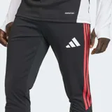 Pantalón de entrenamiento Adidas Tiro 26 Competition, de corte ajustado y color negro con las icónicas tres tiras laterales en color rojo. Presenta un diseño con textura en la parte inferior de las piernas y el logo de la marca en el muslo.