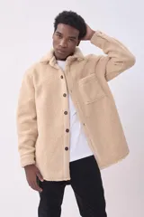 Cazadora de estilo camisa confeccionada en tejido de borreguillo color beige, con cierre frontal de botones, cuello clásico y bolsillo de parche en el pecho.