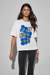 Remera blanca de manga corta y corte oversize, con estampa frontal de flores azules y la inscripción "LET LOVE IN".