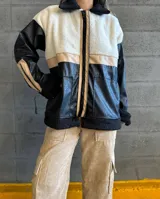 Campera con cuerpo de corderito color beige, mangas y parte inferior de cuero sintético negro con textura tipo cocodrilo. Tiene cuello estilo camisa con solapas de corderito negro, cierre frontal con cremallera y bolsillos laterales.