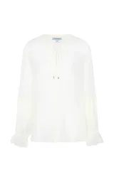 Camisa fluida color blanco marfil con escote en V y cordón ajustable. Cuenta con mangas largas anchas, puños con pliegues y volantes, y dobladillo redondeado.