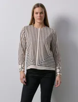 Blusa de gasa estampada con líneas verticales negras sobre fondo beige, de manga larga con puño abotonado. Espalda con abertura y botón.
