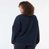 Chaqueta vaquera de corte largo y holgado, color azul oscuro con costuras en contraste. Presenta cuello clásico, cierre frontal con botones metálicos y dos grandes bolsillos frontales de parche.