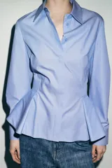 Camisa de algodón con cuello solapa, manga larga con puños y diseño peplum en el bajo. Presenta cierre frontal con botones ocultos por solapa.