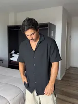 Camisa negra de manga corta, con cuello tipo solapa y textura de punto.