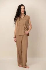 Conjunto compuesto por una blusa sin mangas con cuello camisero, bolsillos frontales y cierre de botones, y un pantalón largo de corte recto y holgado, ambos confeccionados en tejido texturizado de color marrón.
